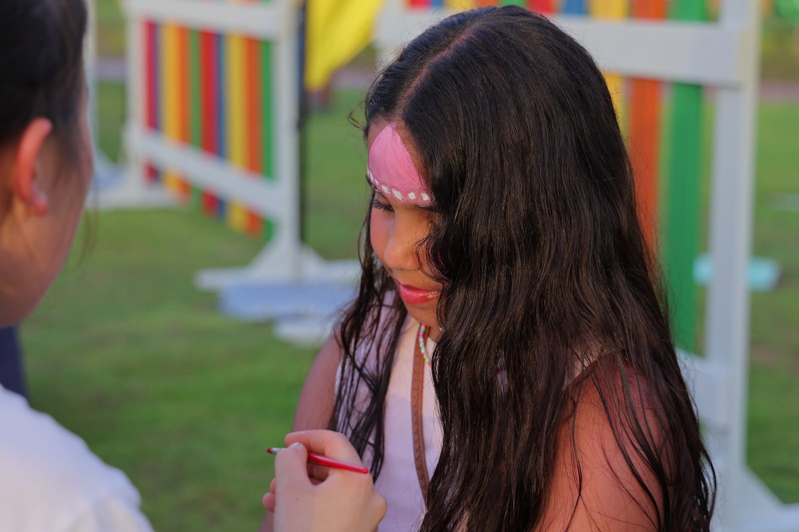 A girl with a painted pink design across her forehead at the face painting table.