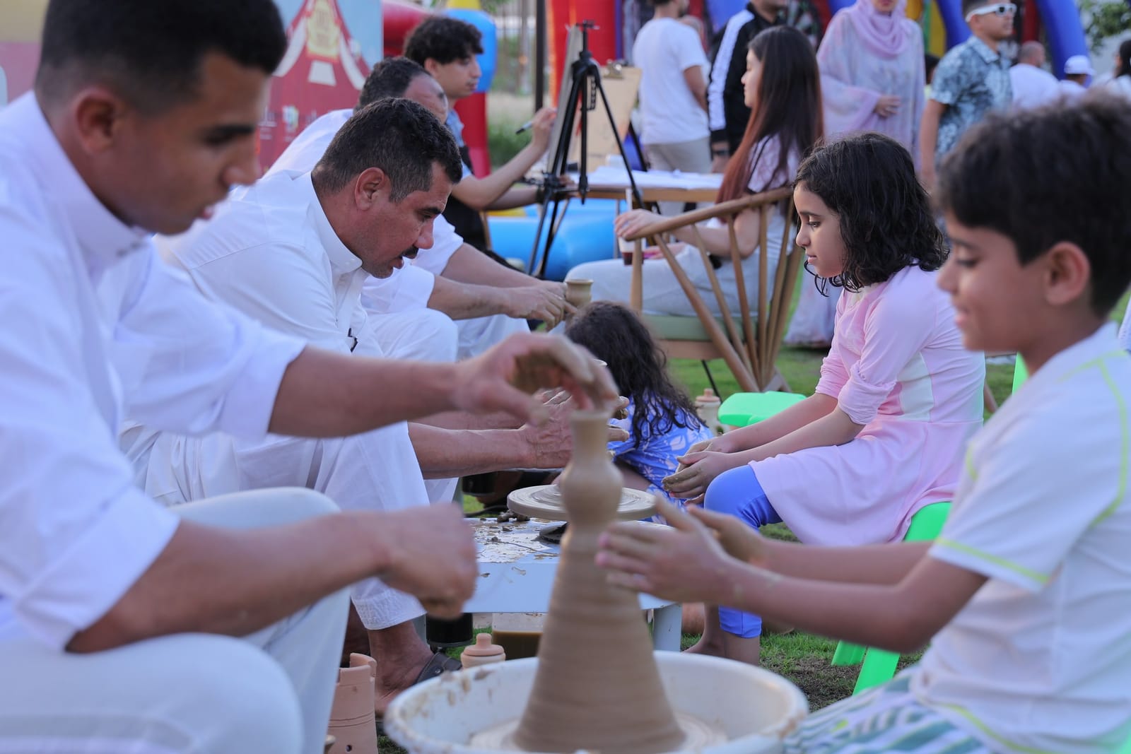 Children and their fathers shaping clay on a pottery wheel at the carnival workshop.