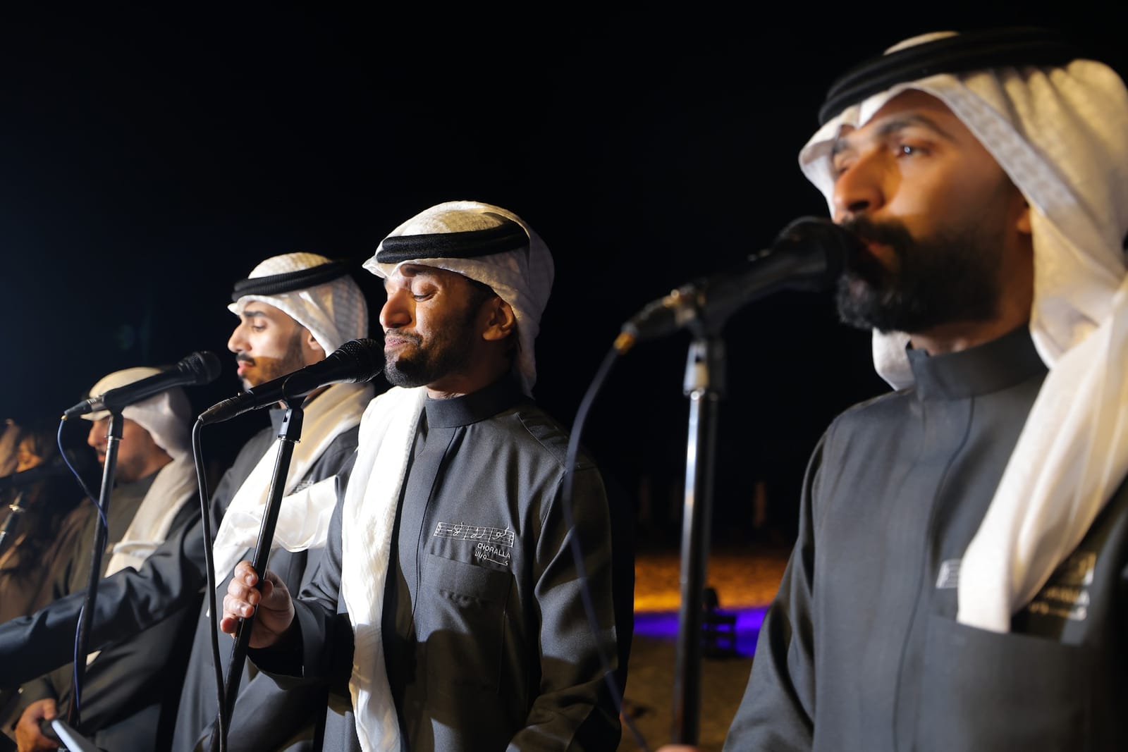 A men's vocal group in traditional dress singing at microphones at night.