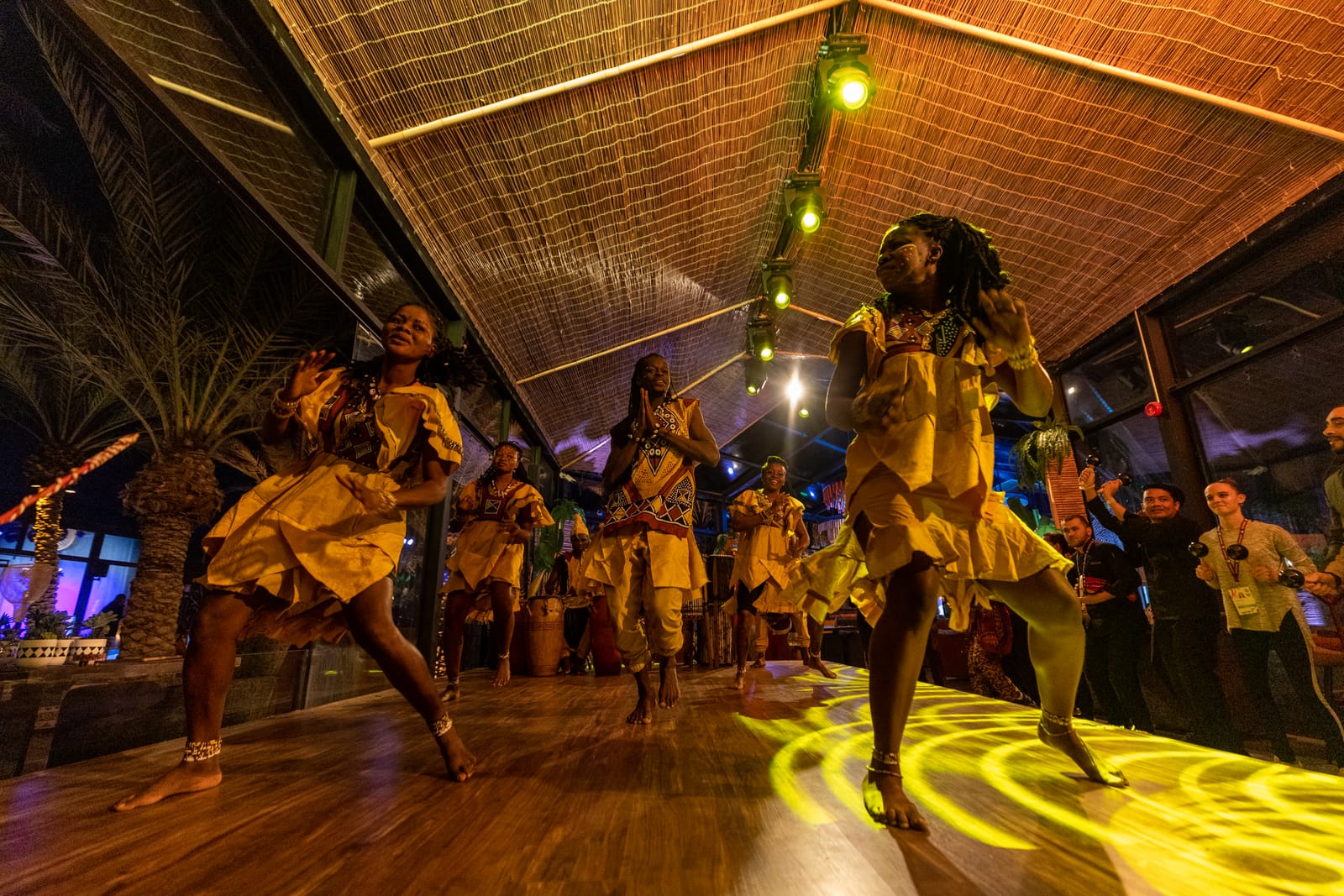 Dancers in yellow performing on a wooden floor at Zamazolo, with guests gathered around them.