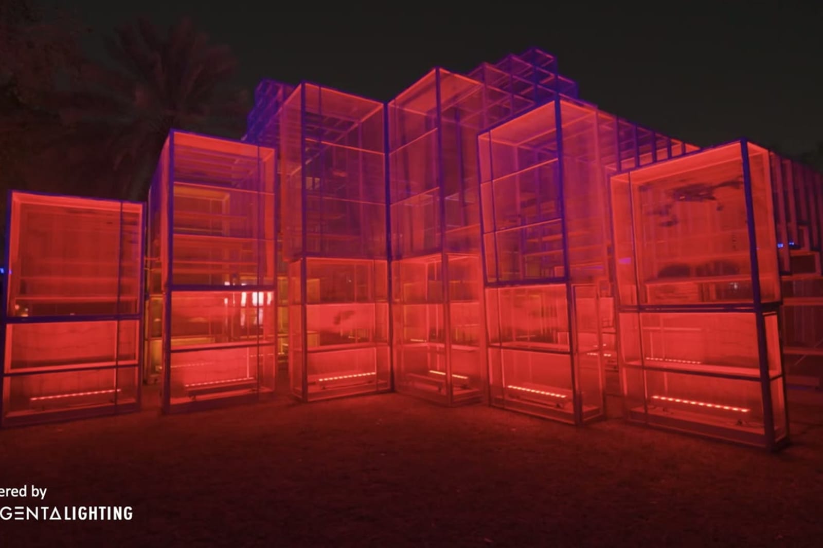 The same sculpture lit deep red, its mesh volumes glowing against the night.